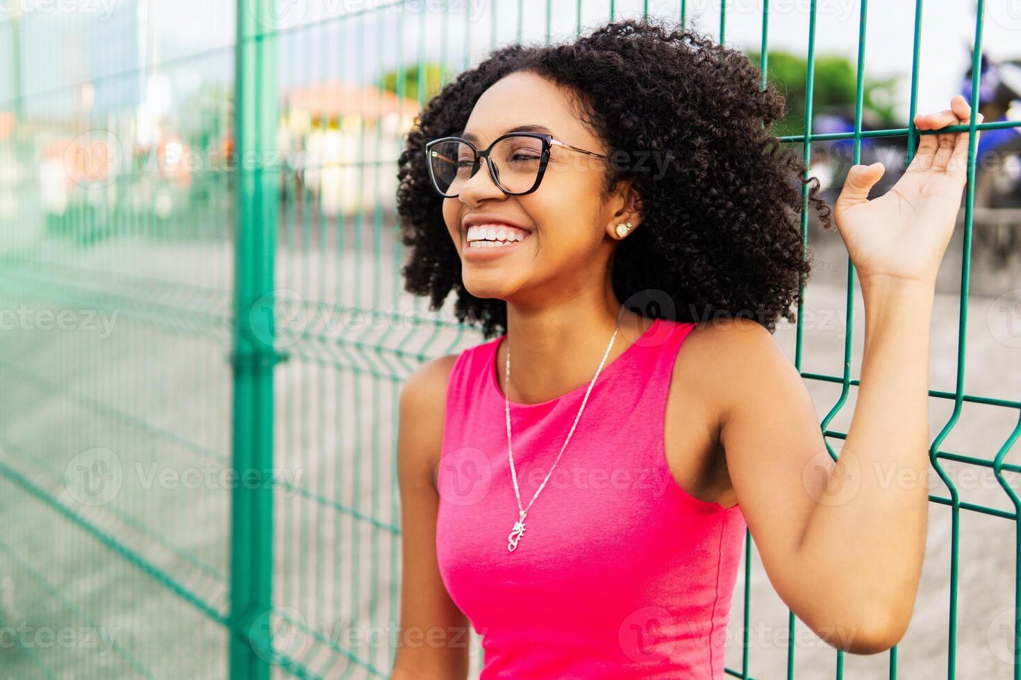 Close up studio shot of beautiful young mixed race woman model with curly dark hair looking at camera with charming cute smile while posing against white blank copy space wall for your content photo