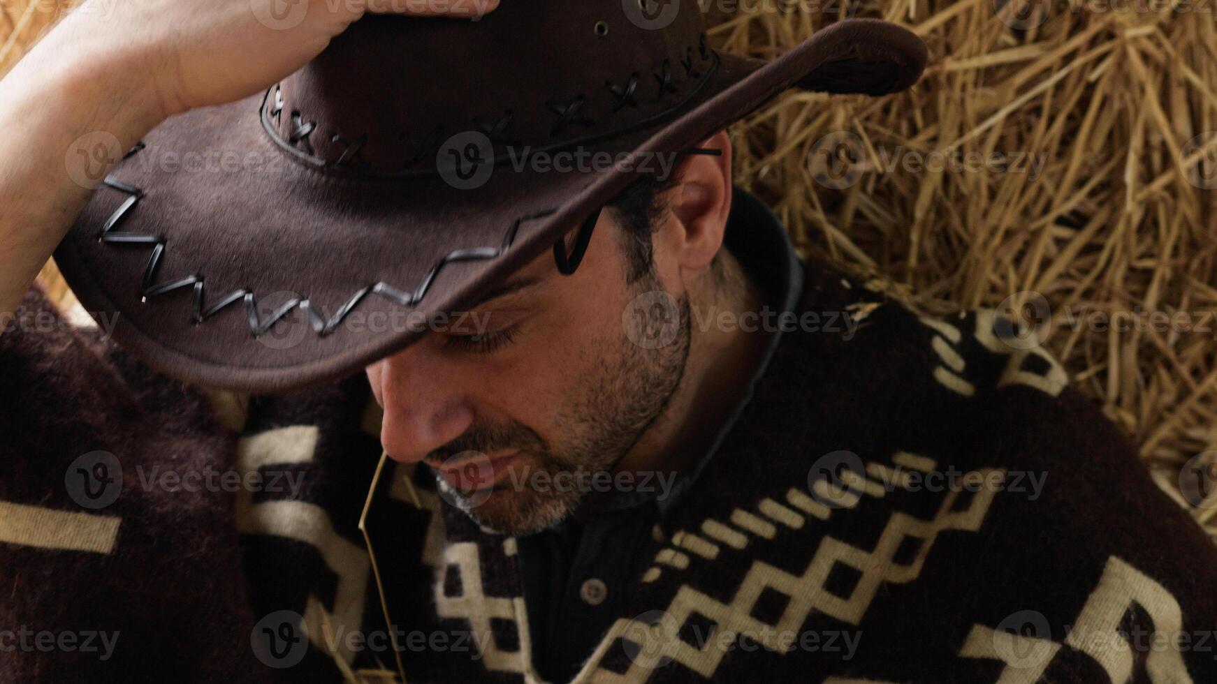 Tired cowboy leaning on hay bale photo