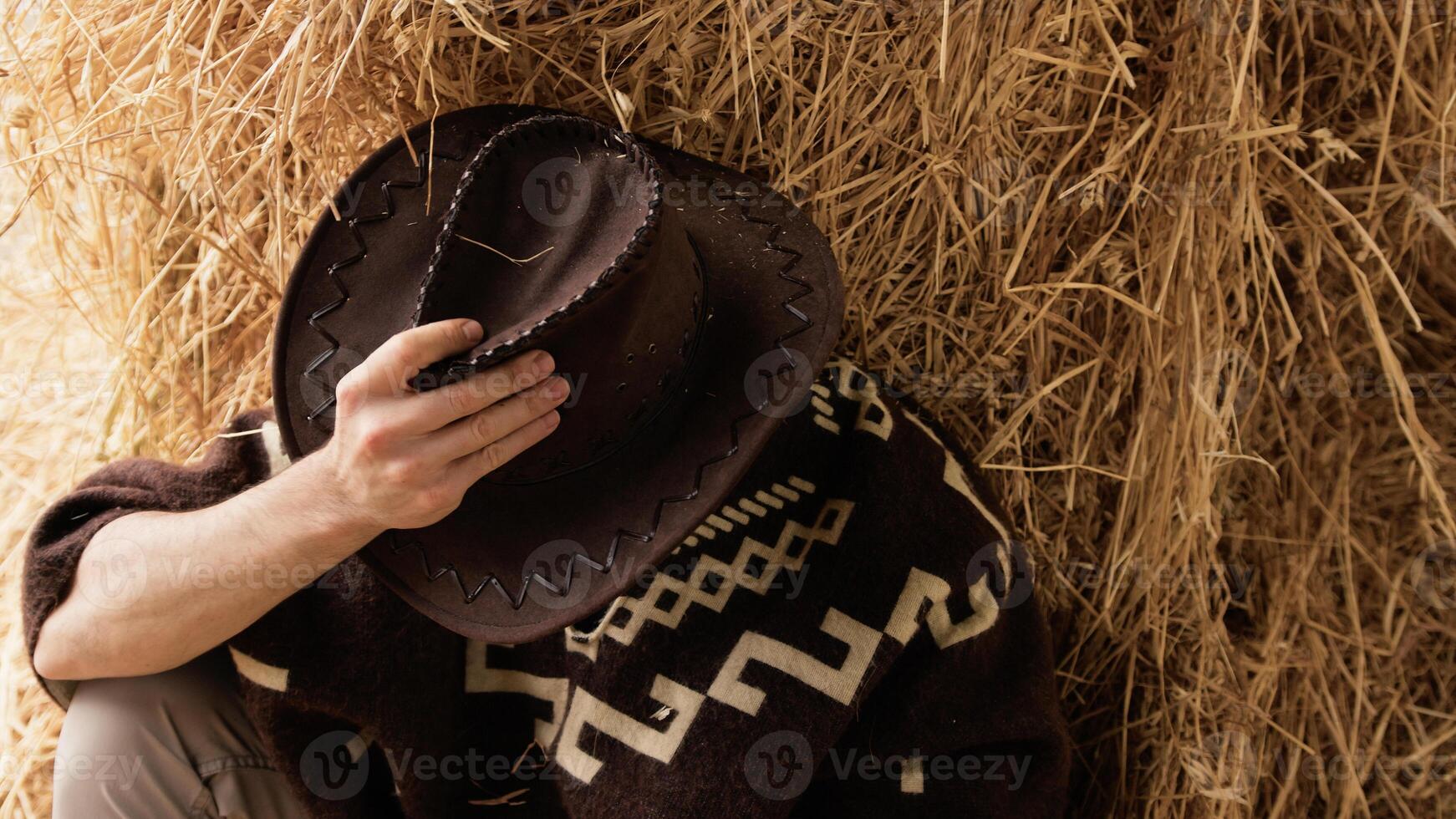 Tired cowboy leaning on hay bale photo
