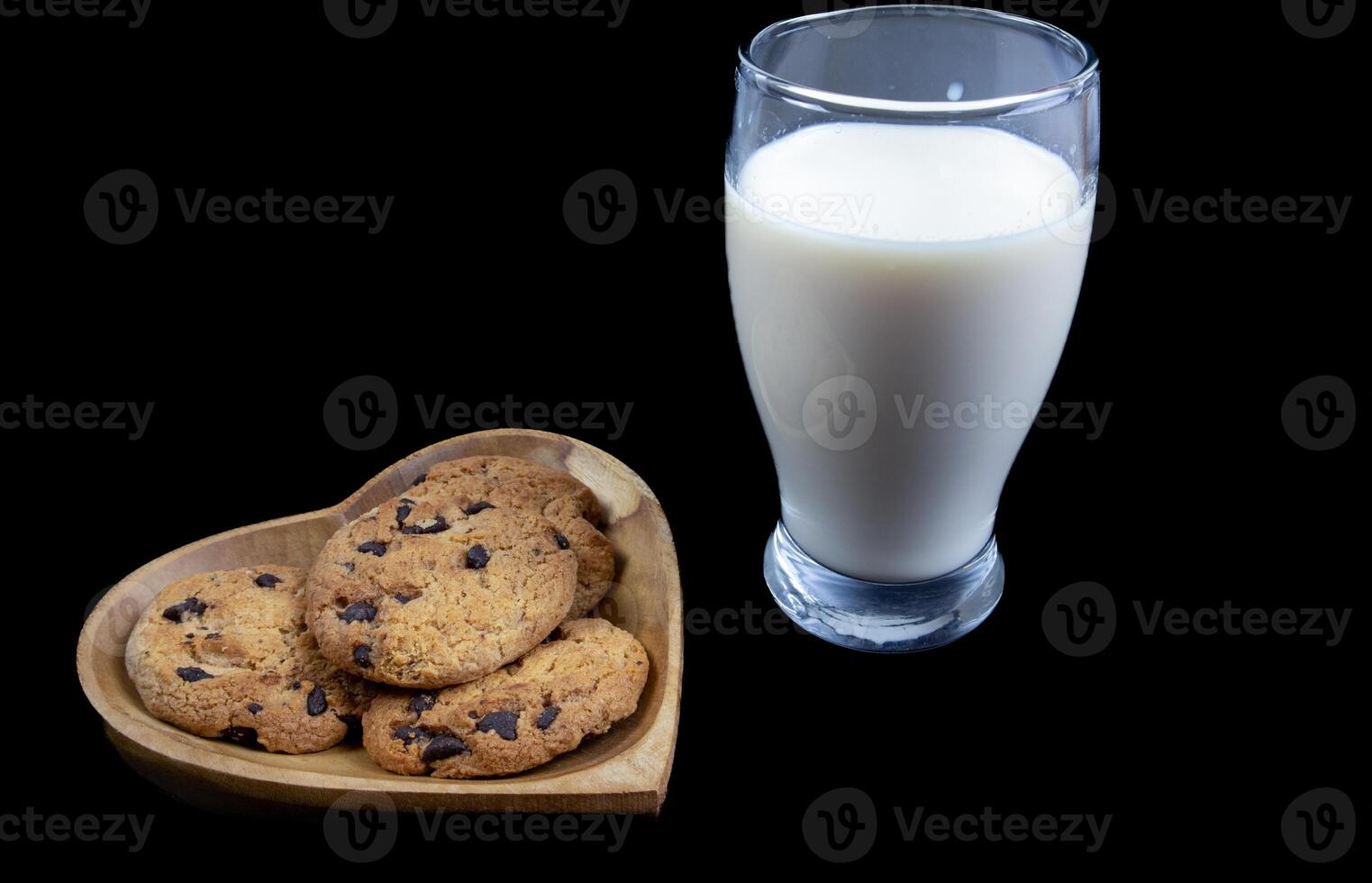 Chocolate chip cookies on a heart shaped plate with a glass of fresh milk on black background photo