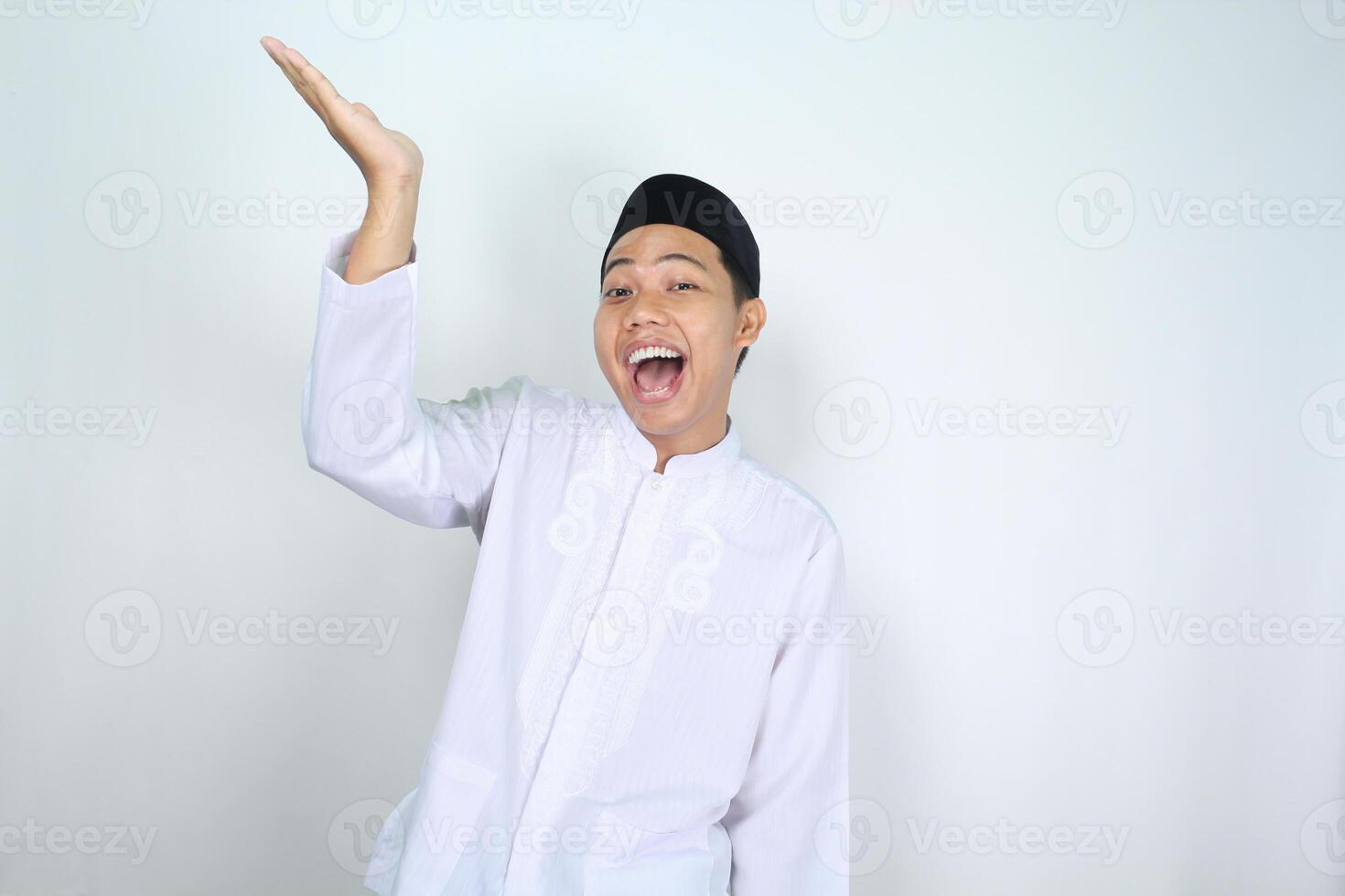 cheerful muslim asian man screaming while raising hand to presenting empty space above isolated on white background photo