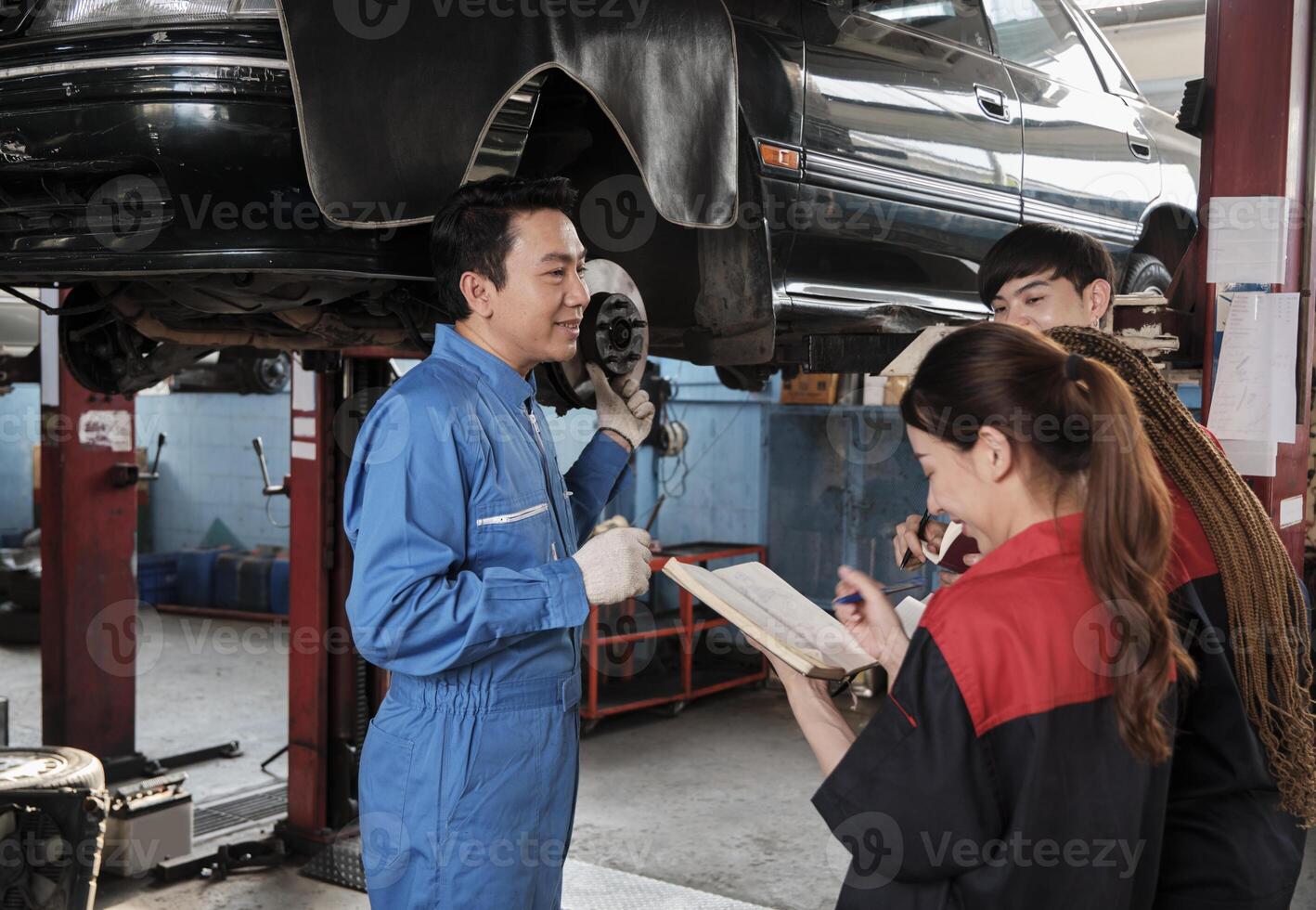 asiático masculino profesional automotor ingeniero supervisor describe coche rueda y suspensión reparar trabajo con mecánico trabajador personal equipo en reparar Servicio cochera, especialista ocupaciones en auto industria. foto