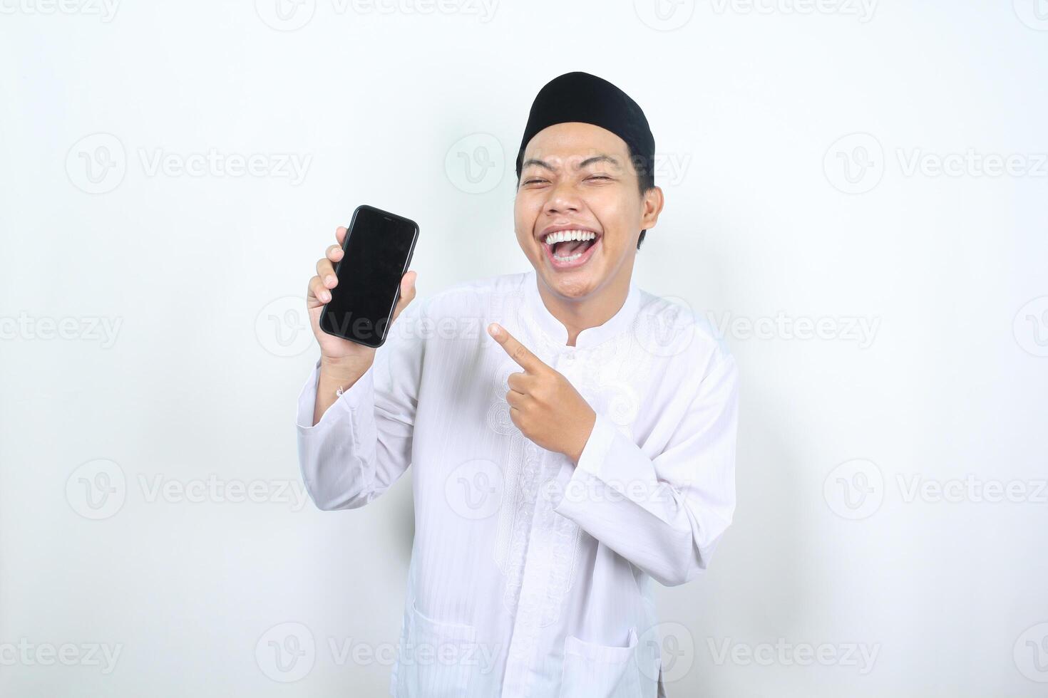 happy asian muslim man laughing while pointing to blank phone screen photo