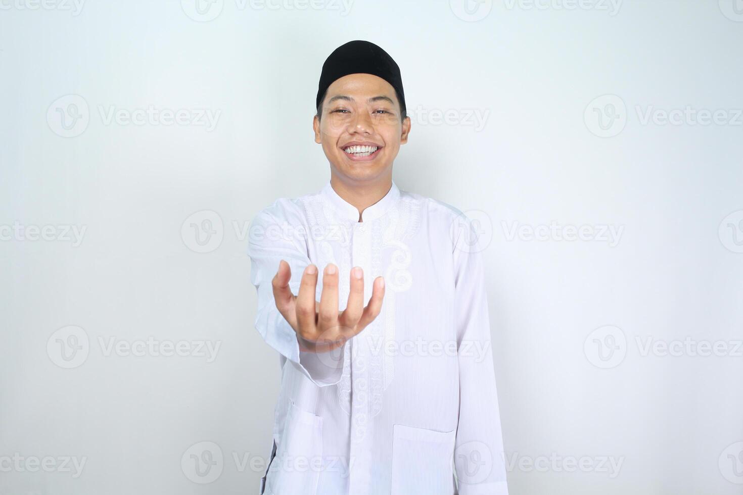 smiling asian muslim man showing empty palm at camera holding imaginary food plate isolated on white background photo