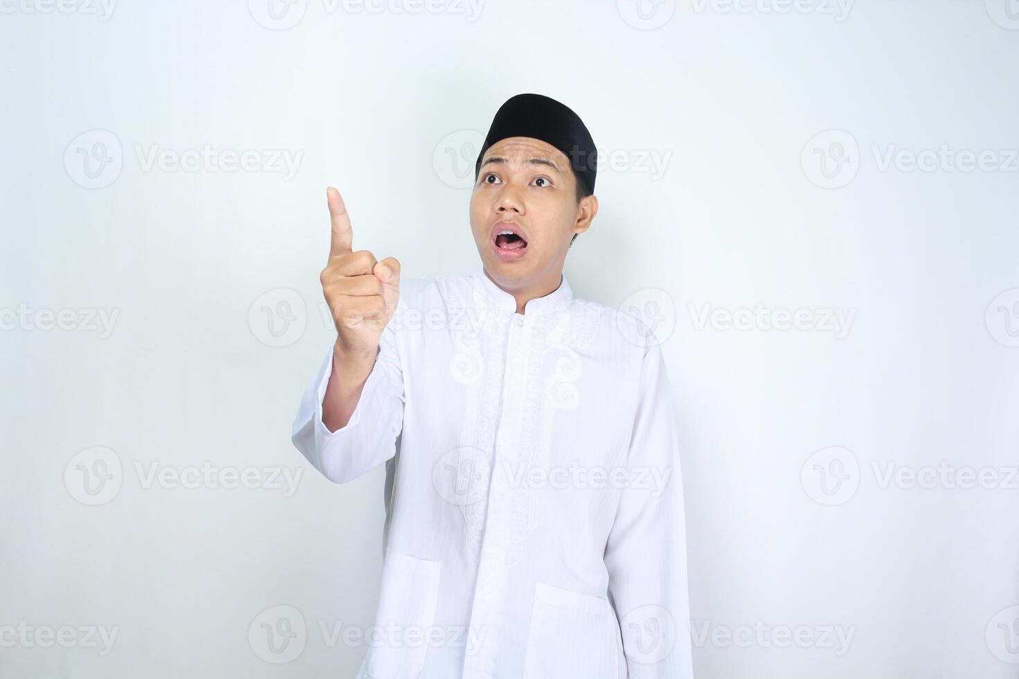muslim asian man pointing beside with shocked expression isolated on white background, looking at camera photo