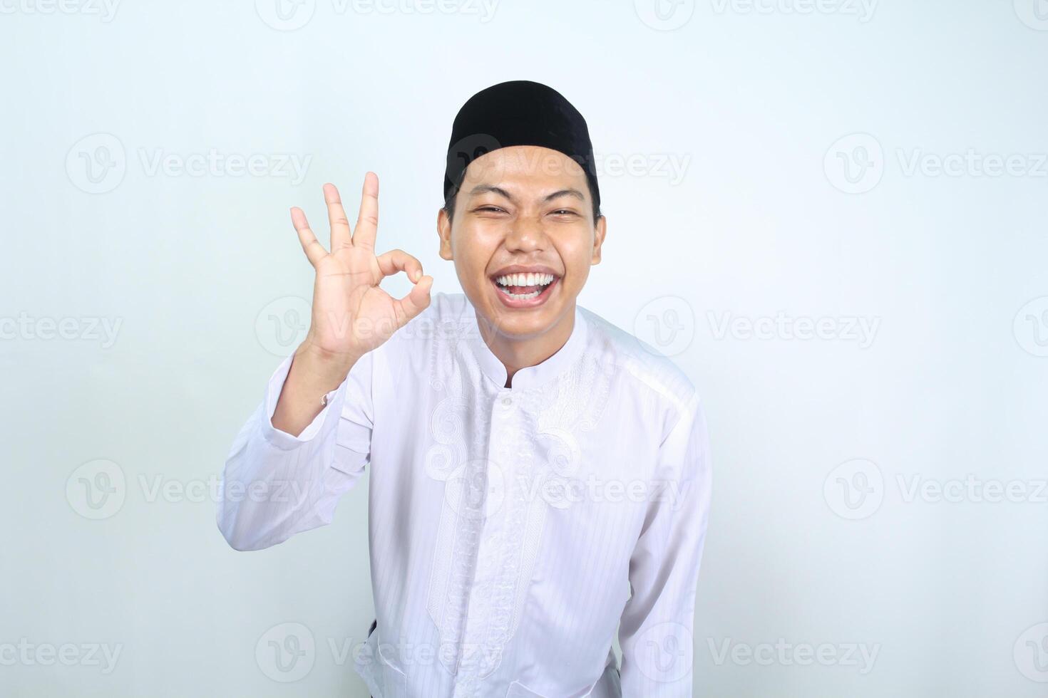 joyful asian muslim man show ok sign with laughing expression isolated on white background photo