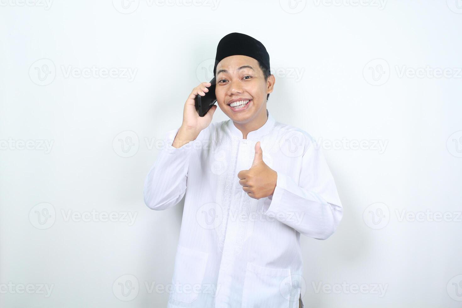 sonriente musulmán asiático hombre demostración pulgares arriba mientras vocación con su móvil teléfono aislado foto