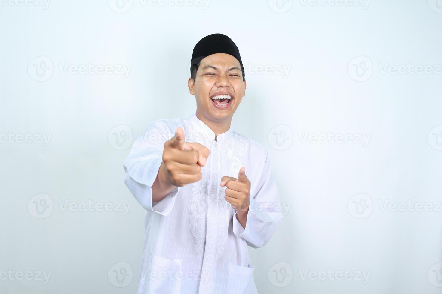 laughing asian muslim man pointing at camera isolated on white background photo