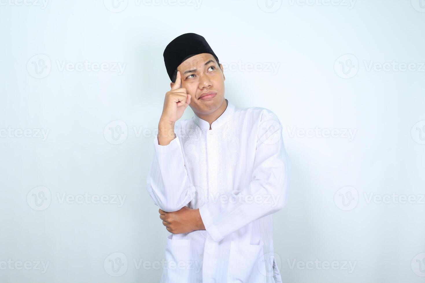 thoughtful asian muslim man looking above with hand touching his head isolated on white background photo