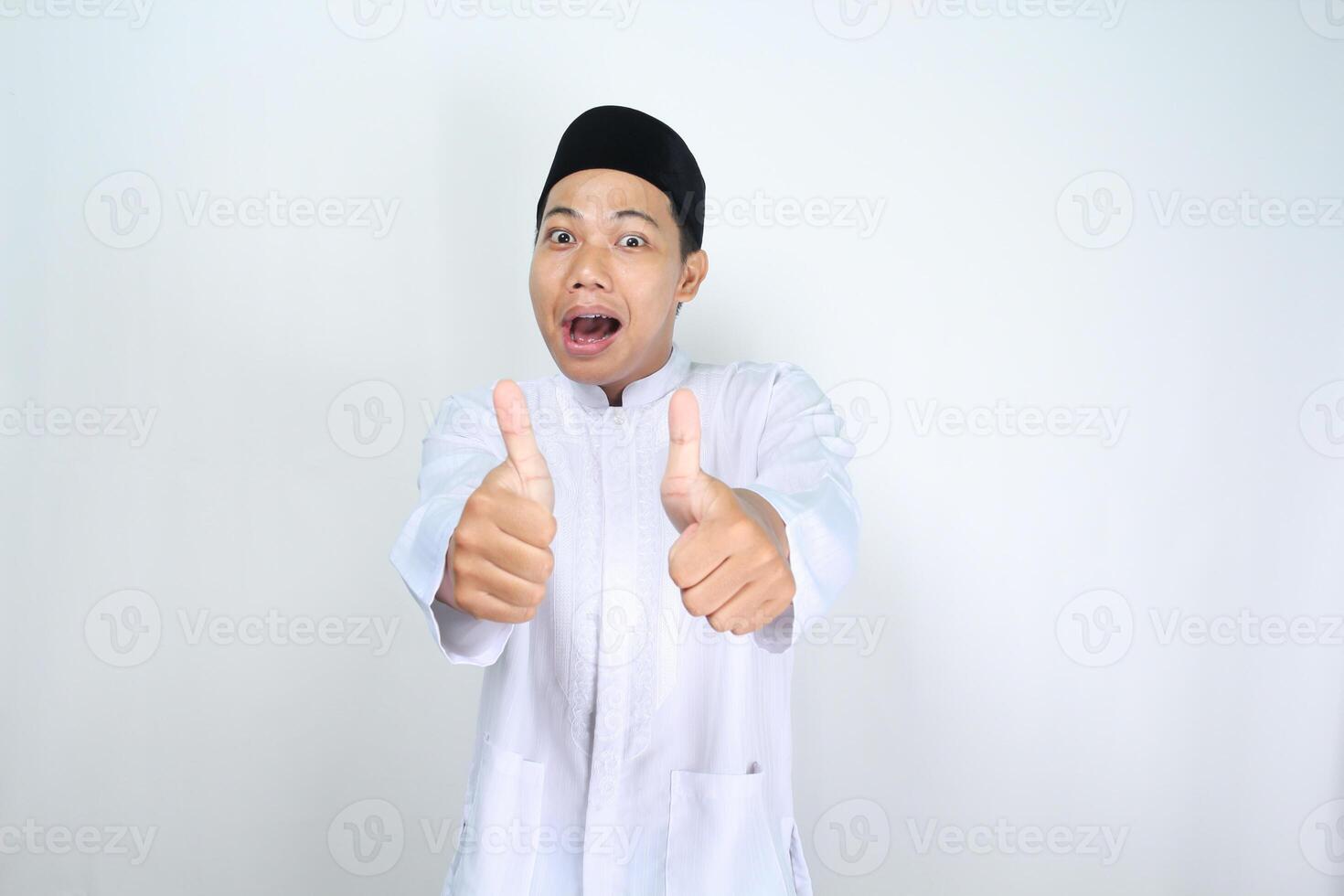 funny asian muslim man giving thumbs up with surprised expression isolated on white background photo