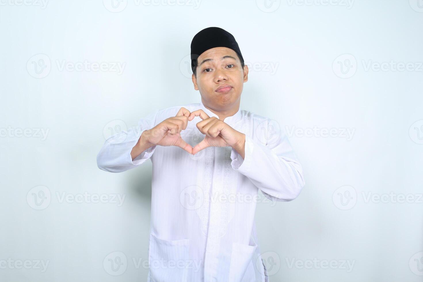 unhappy asian muslim man looking at camera and show heart shape isolated on white background photo