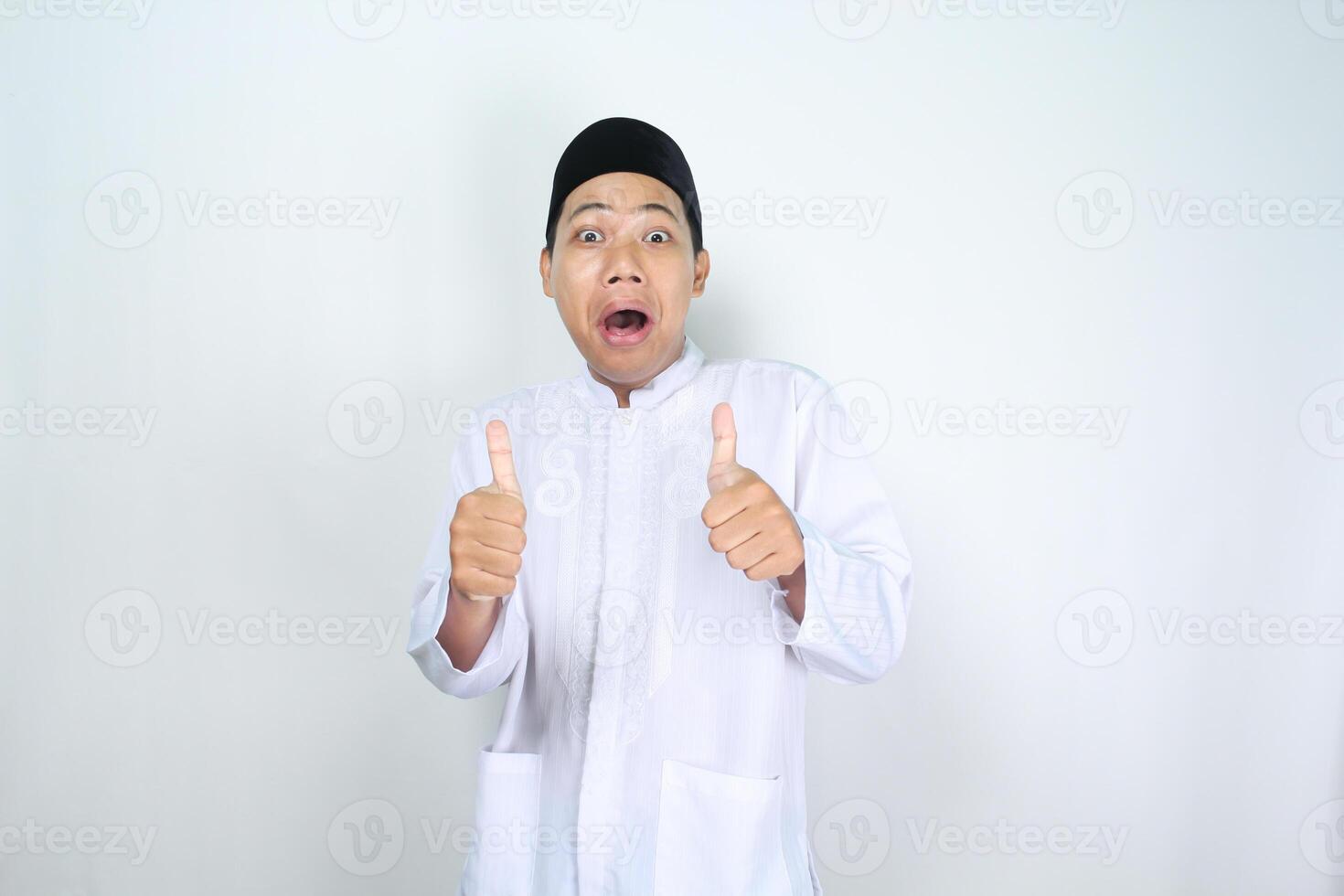 funny asian muslim man giving thumbs up with surprised expression isolated on white background photo