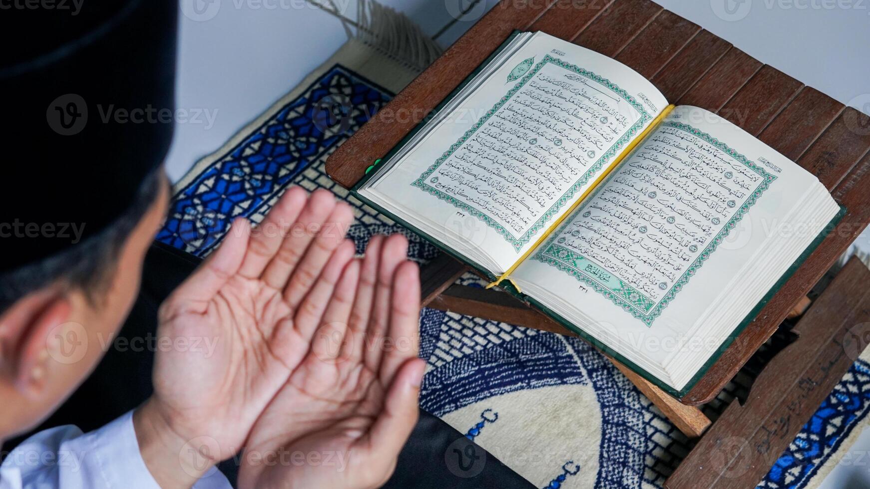 close up photo of a Muslim man reading the Quran on a prayer mat during the holy month of Ramadan.