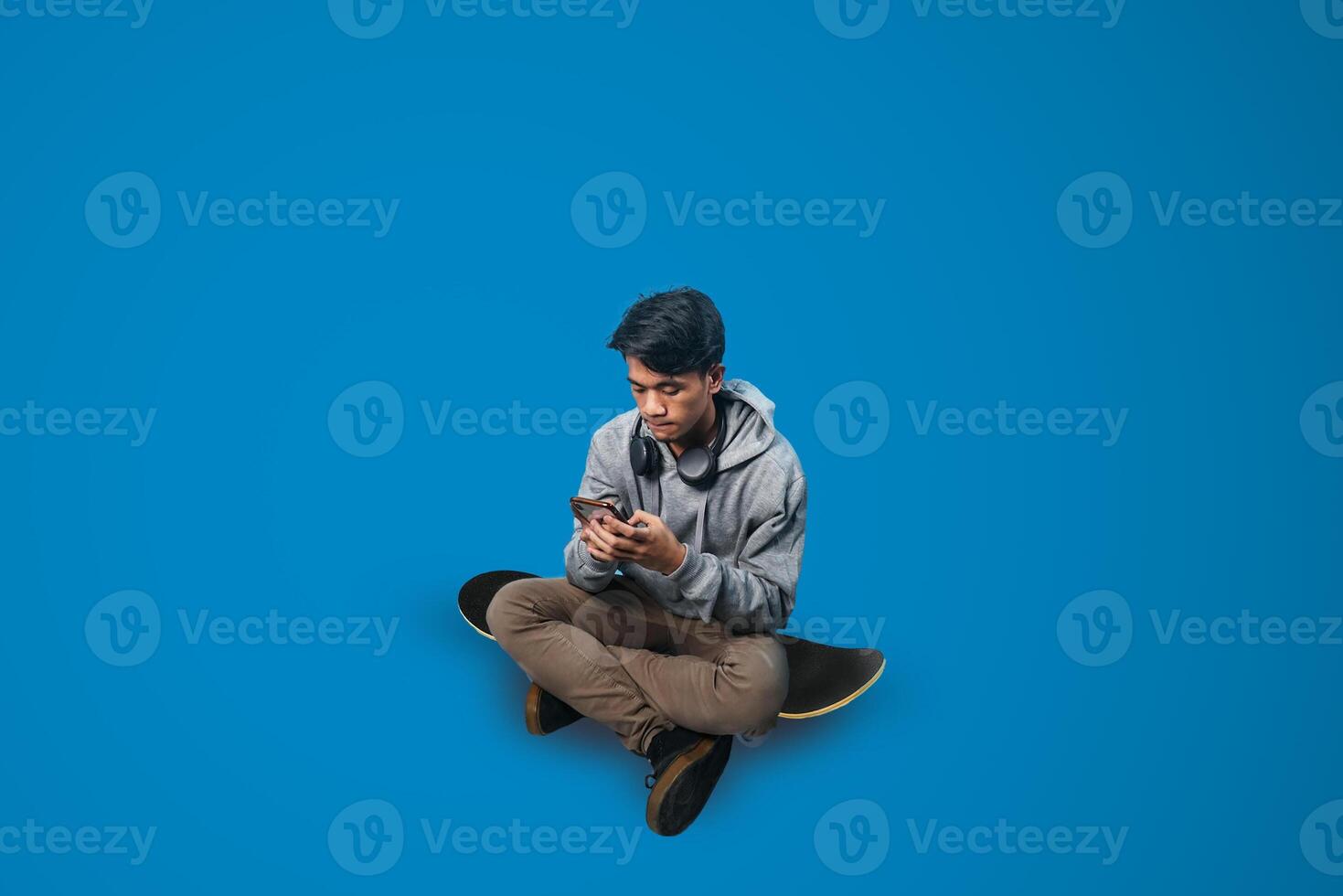 a student is sitting holding a smartphone on a skateboard with a blue background photo