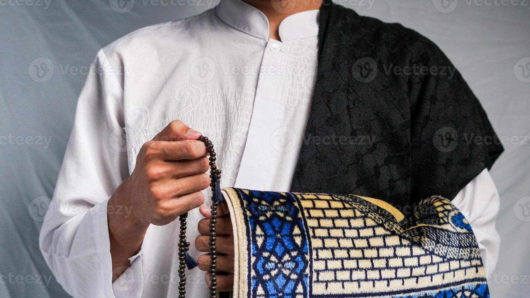 man is praying with prayer beads and carrying a prayer mat photo