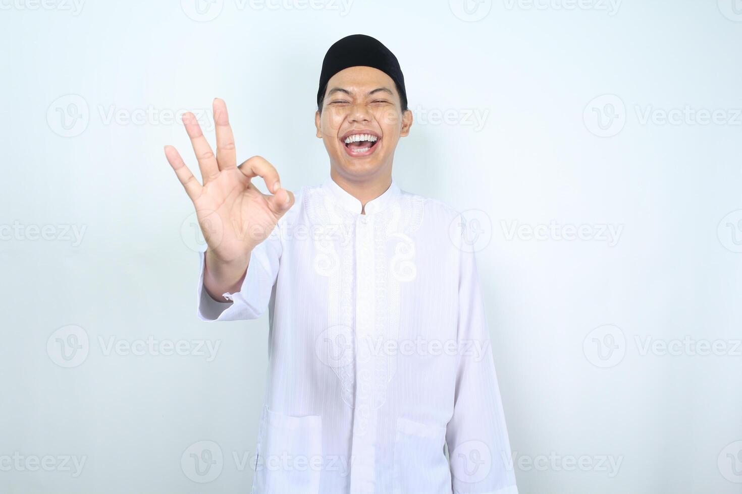 joyful asian muslim man show ok sign with laughing expression isolated on white background photo