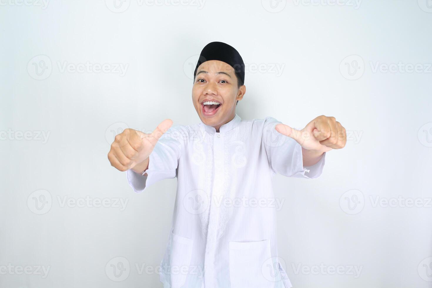 funny asian muslim man giving thumbs up with surprised expression isolated on white background photo