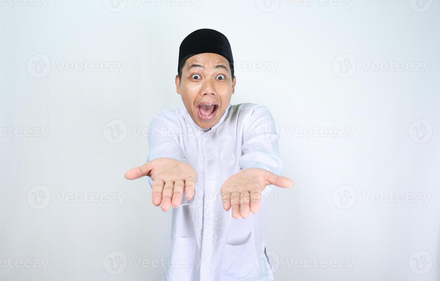 funny asian muslim man with surprised expression presenting hand forward to camera isolated on white background photo