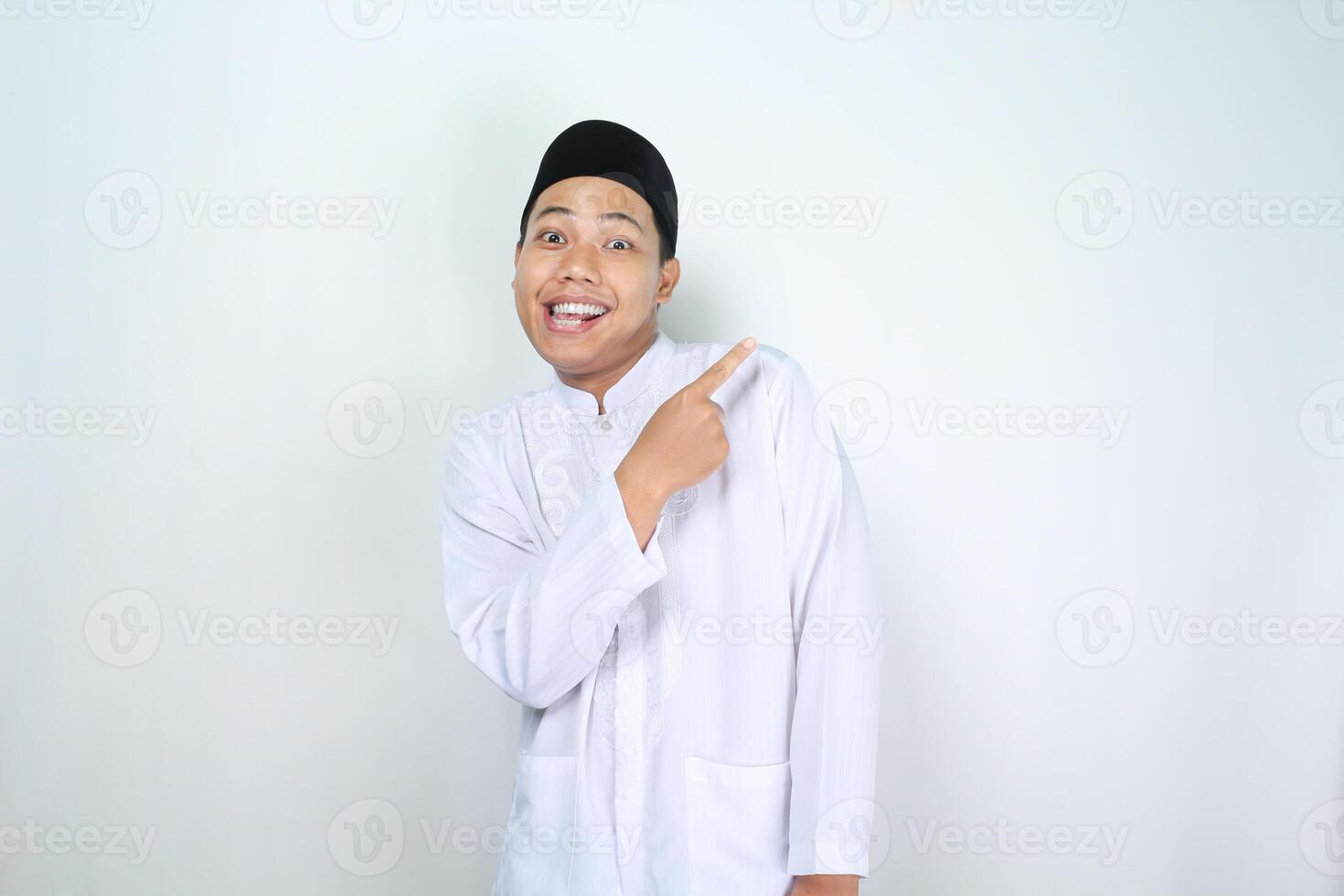 surprised asian muslim man pointing to copy space isolated on white background photo