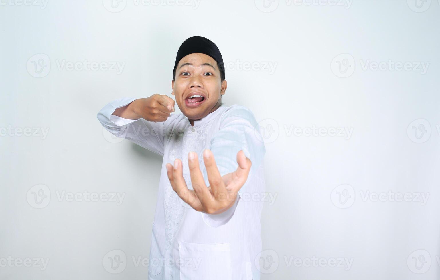 funny asian muslim man pointing to empty palm posing holding bowl isolated on white background photo