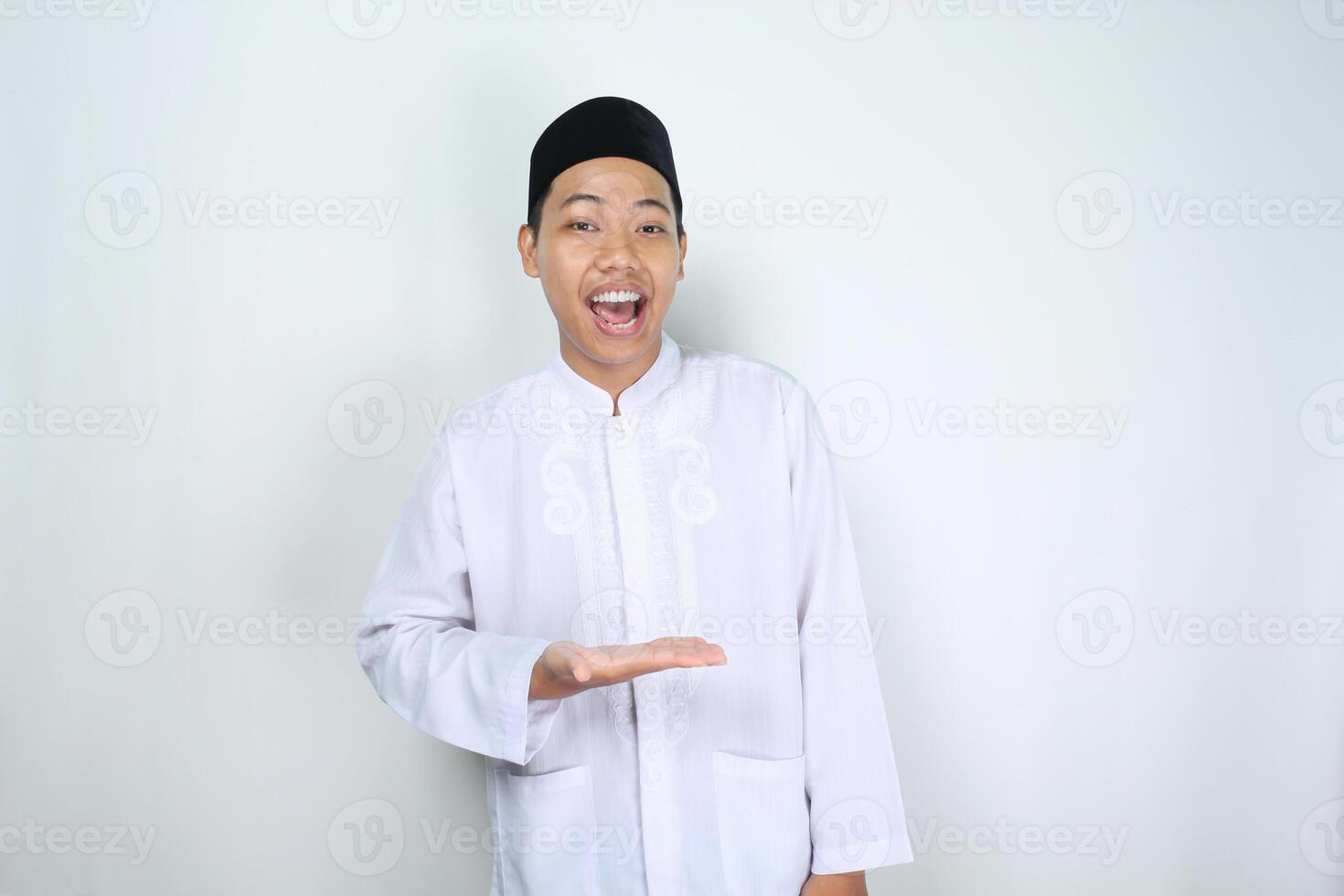 cheerful muslim asian man screaming while showing empty palm over his chest to presenting isolated on white background photo