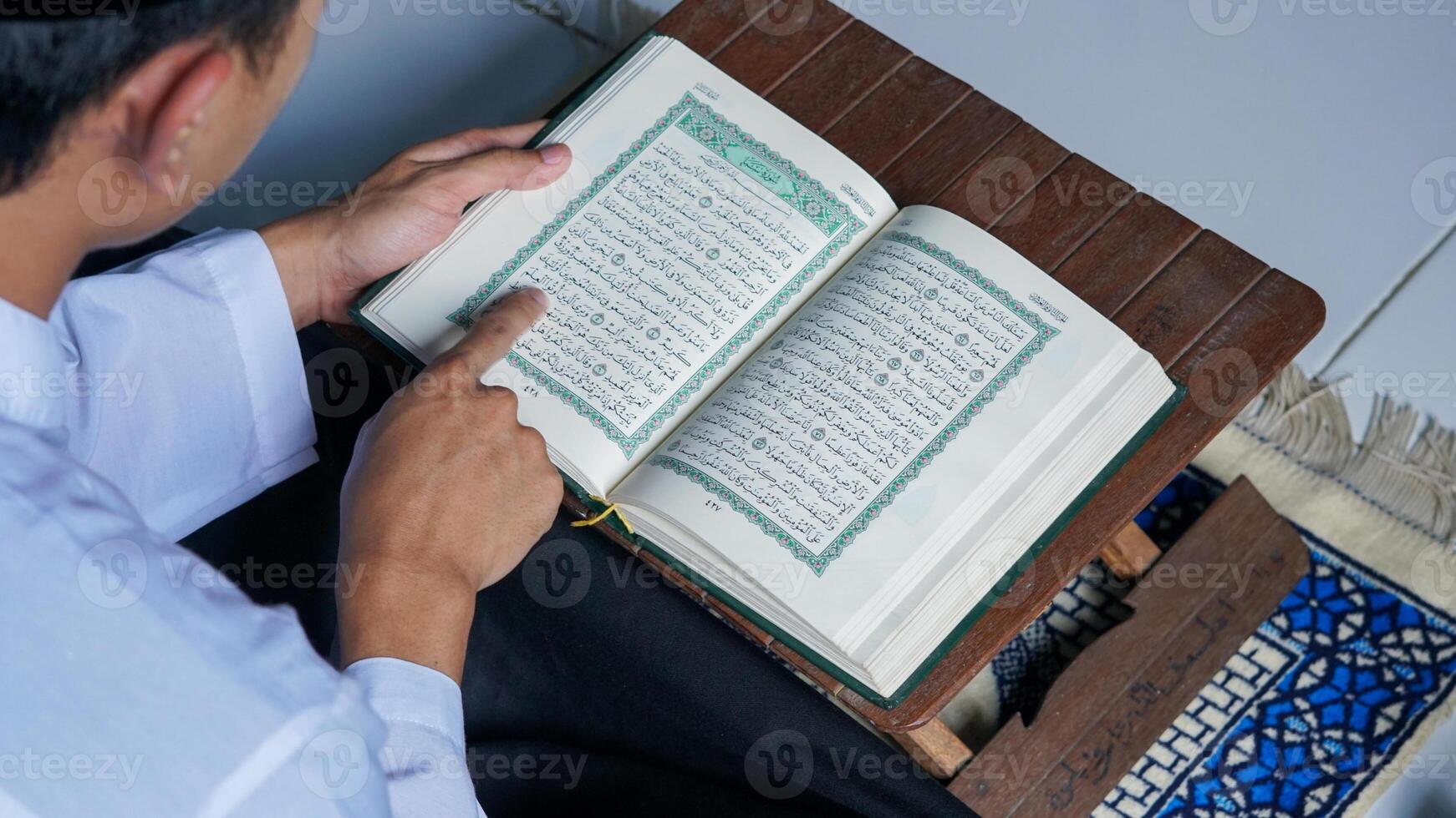 close up photo of a Muslim man reading the Quran on a prayer mat during the holy month of Ramadan.