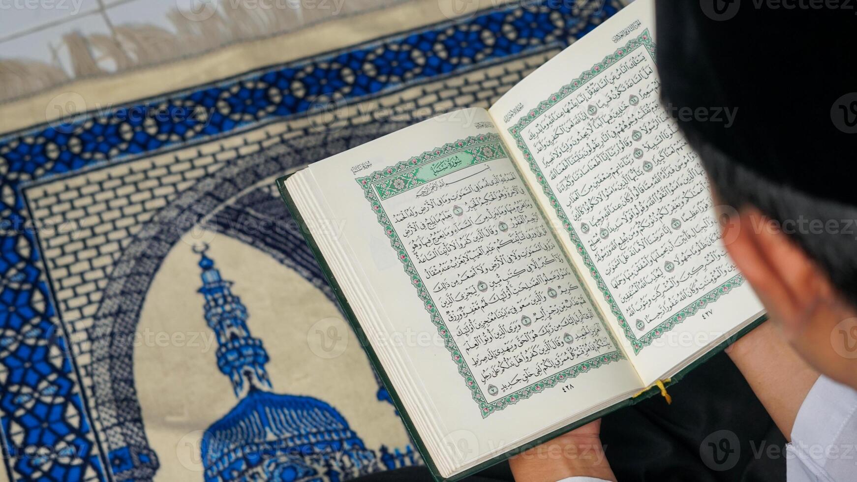 close up photo of a Muslim man reading the Quran on a prayer mat during the holy month of Ramadan.