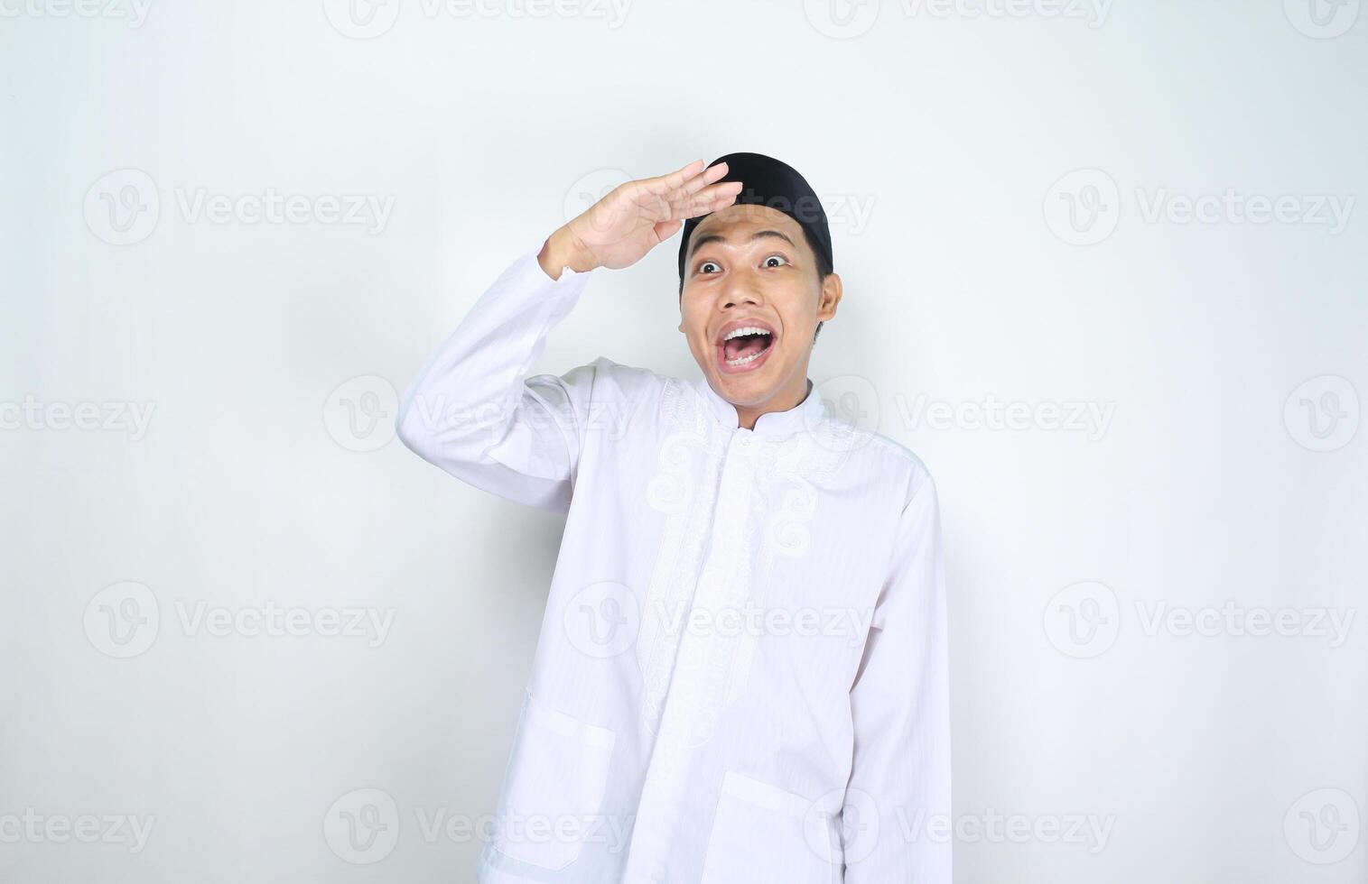 gracioso musulmán hombre asiático espectáculo sorprendido expresión mientras mirando lejos lejos con mano elevado terminado su cabeza aislado en blanco antecedentes foto
