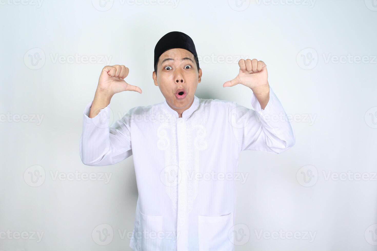 conmocionado asiático hombre musulmán señalando a él yo con su pulgares aislado en blanco antecedentes foto