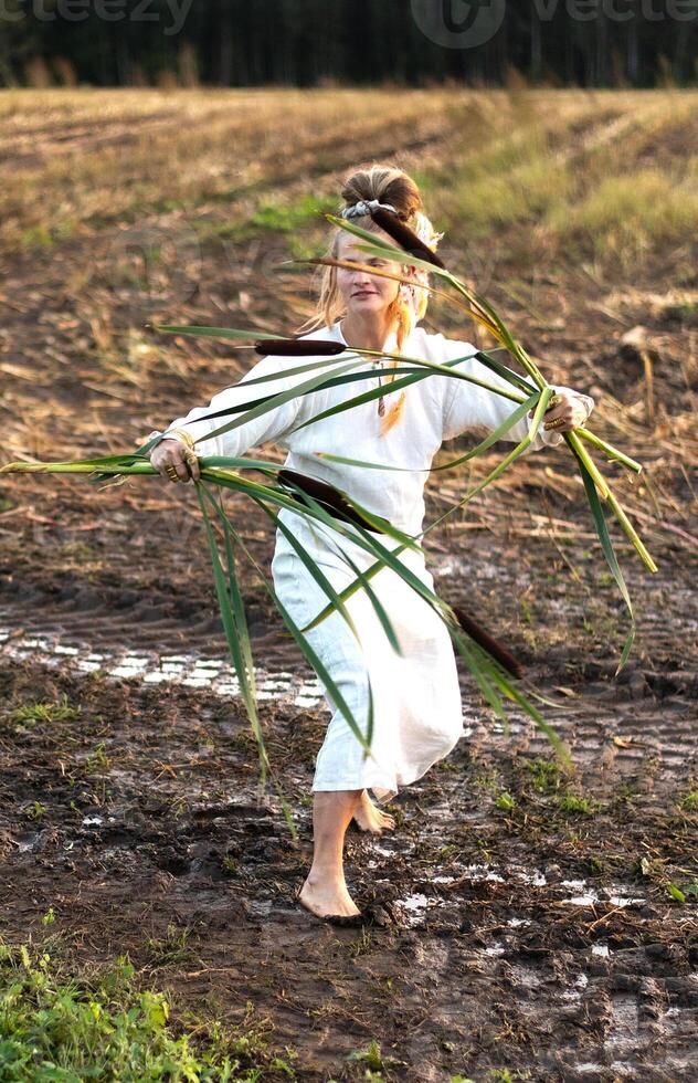 Cheerful young  woman with reeds dances in colored smoke in a field. photo