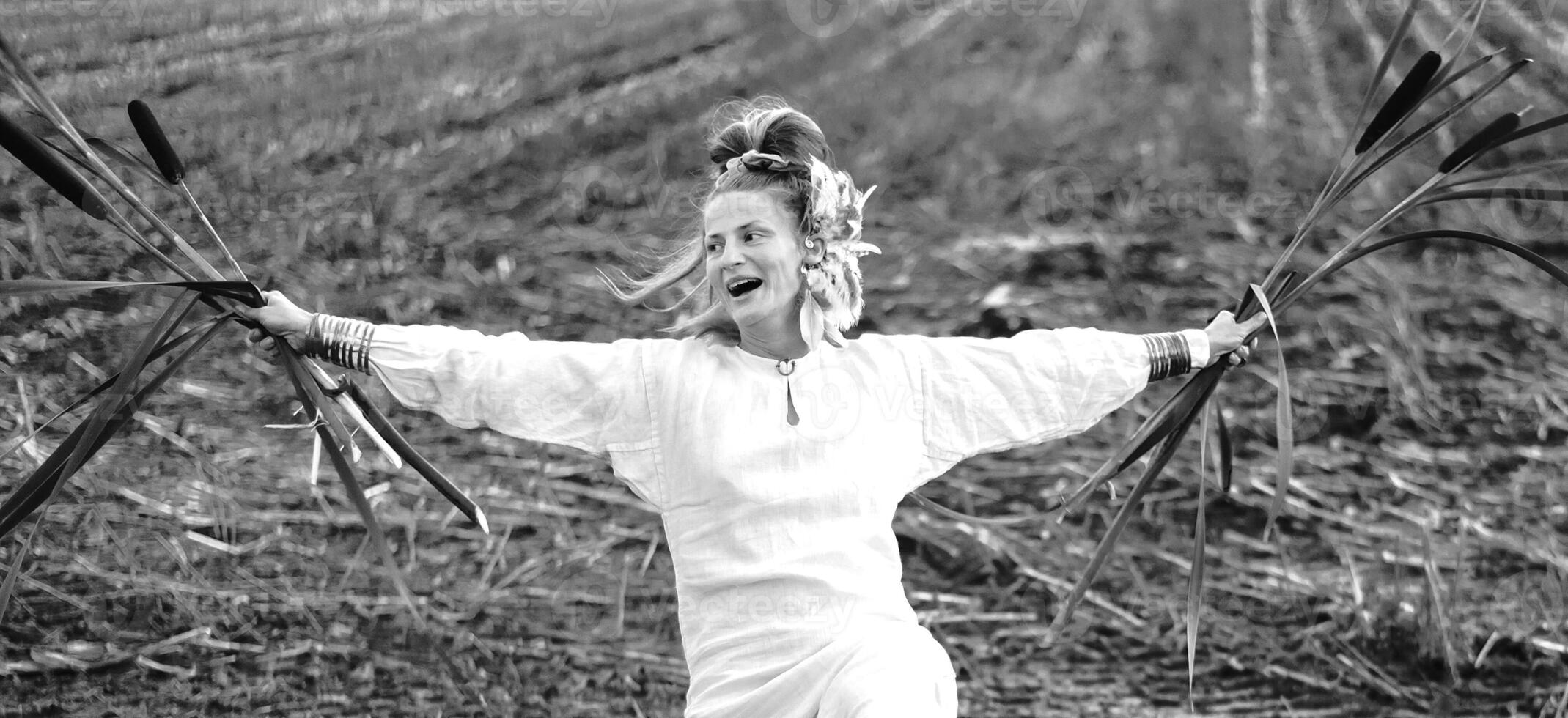 Cheerful young  woman with reeds dances in colored smoke in a field. photo