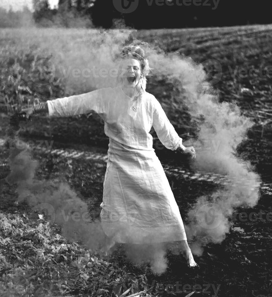 alegre joven mujer con cañas bailes en de colores fumar en un campo foto