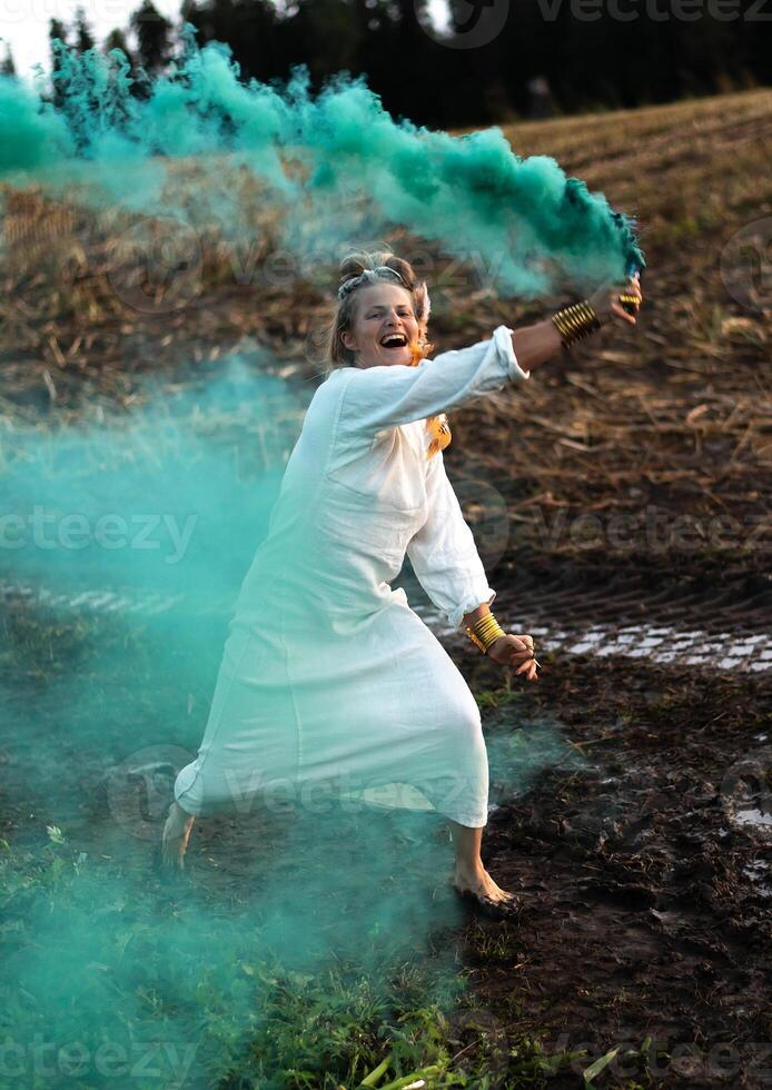 Cheerful young  woman with reeds dances in colored smoke in a field photo