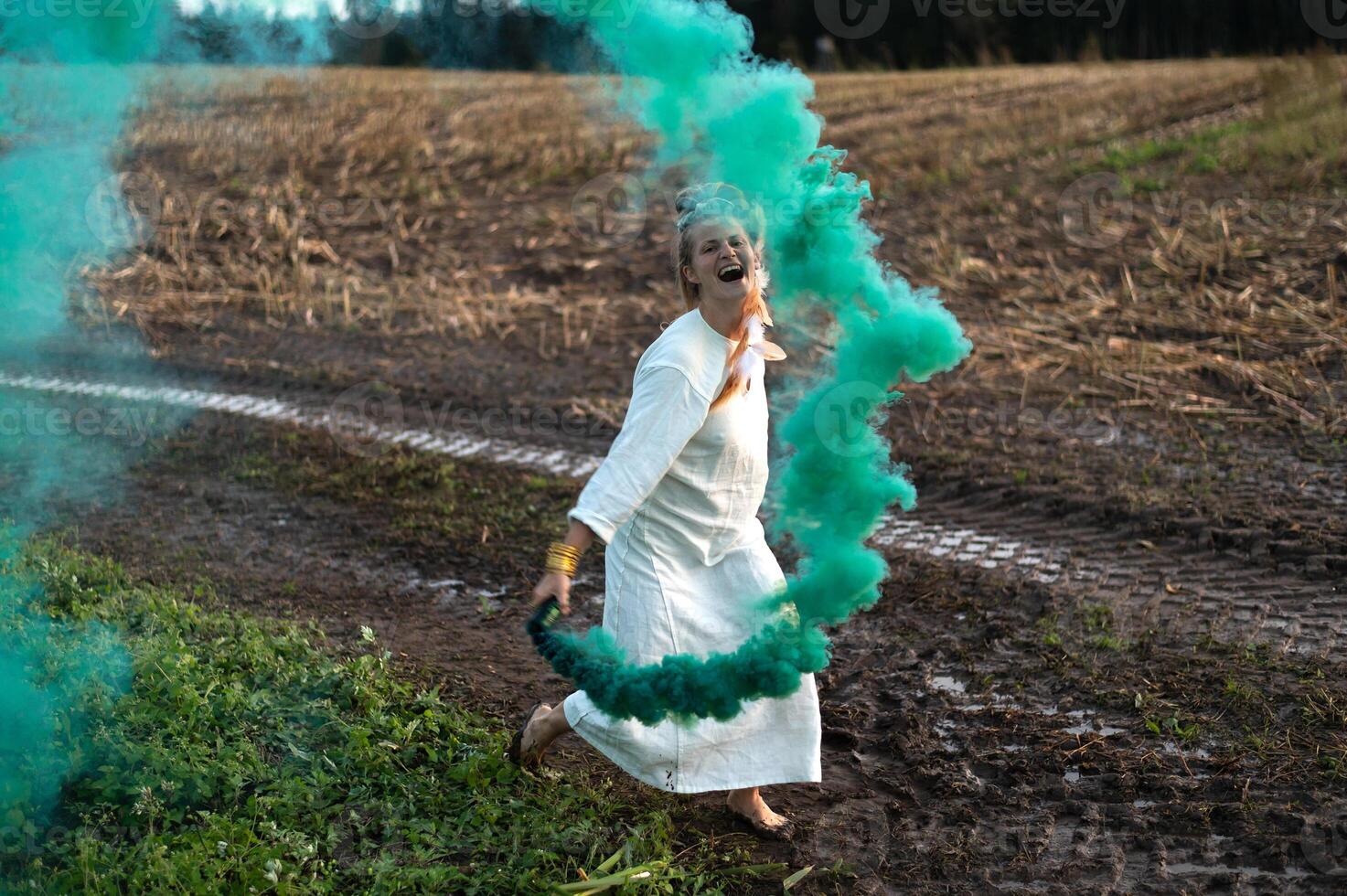 Cheerful young  woman with reeds dances in colored smoke in a field photo