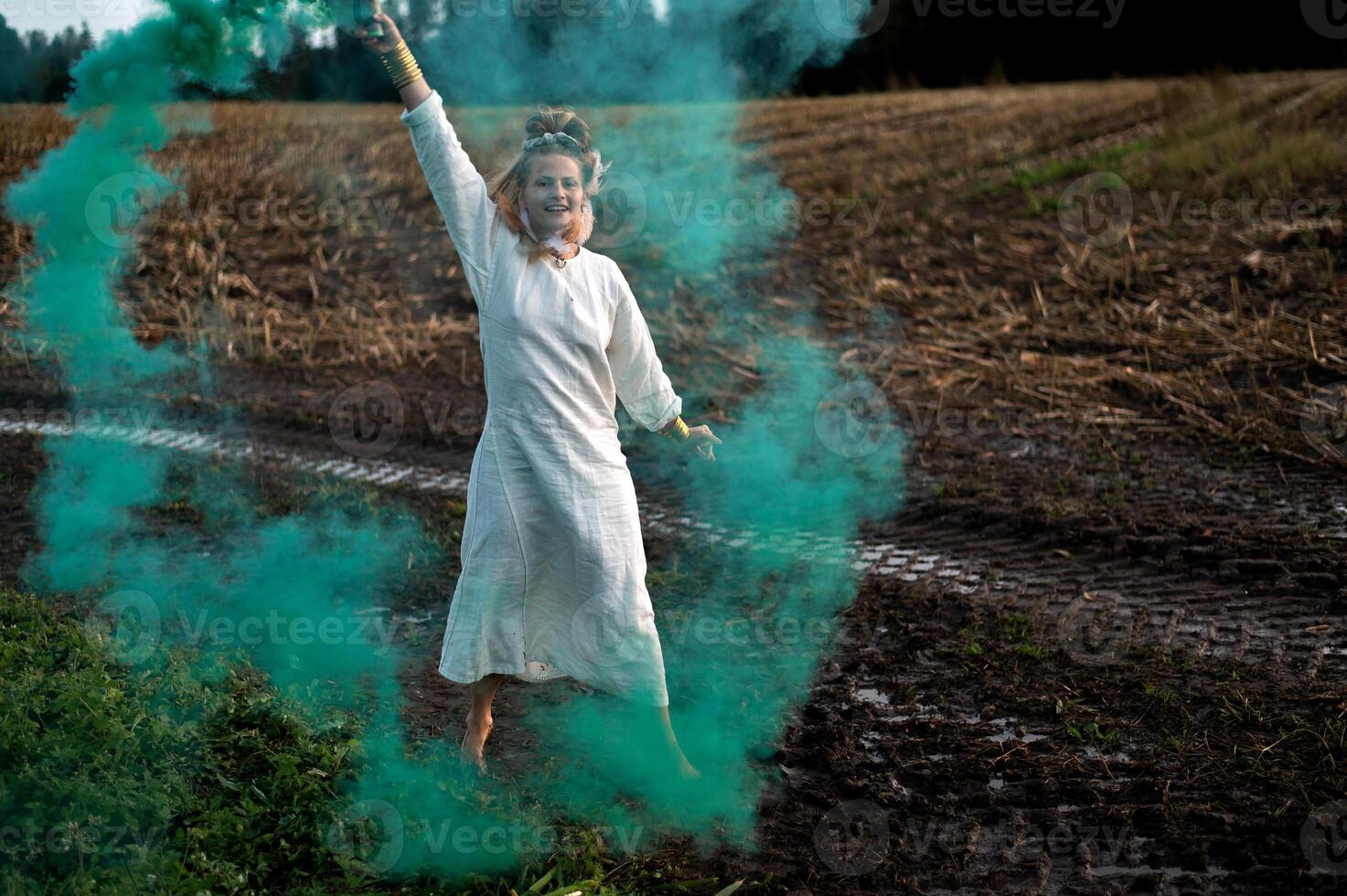 Cheerful young  woman with reeds dances in colored smoke in a field photo