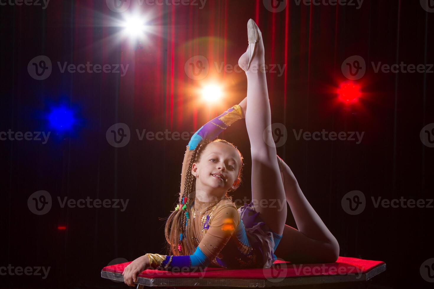 A girl with a flexible body. Performs a circus artist. Circus gymnast. Balancing act. The child performs an acrobatic trick photo