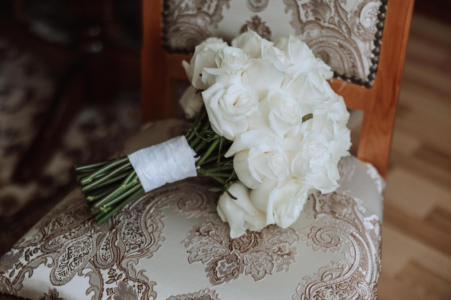 Wedding bouquet. White cut roses, green seed heads and leaves. Green stems and white ribbon and gold wedding rings. photo