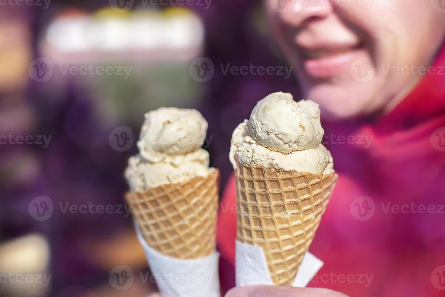 Creme brulee ice cream in a waffle cup against a background of a blurred person and purple bokeh spots. photo
