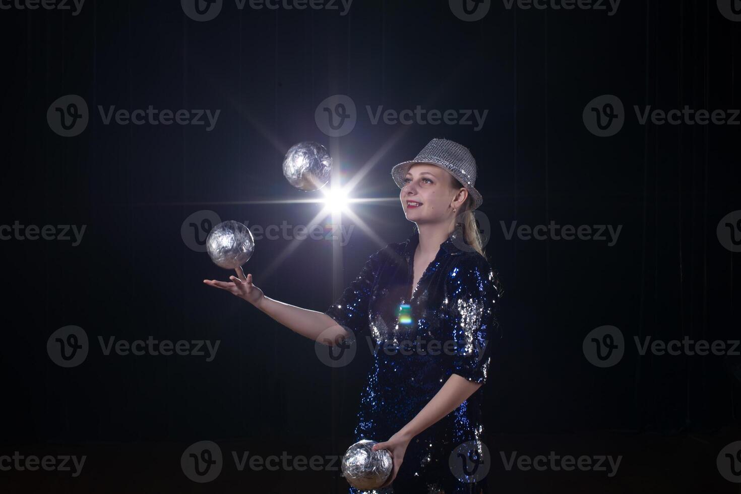 Circus actress performs. The girl juggles balls on a dark background in the spotlights. photo