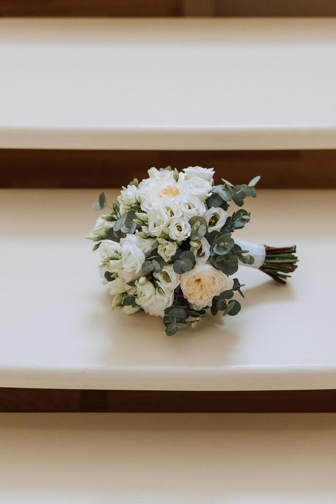 Wedding bouquet. White cut roses, green seed heads and leaves. Green stems and white ribbon and gold wedding rings. photo