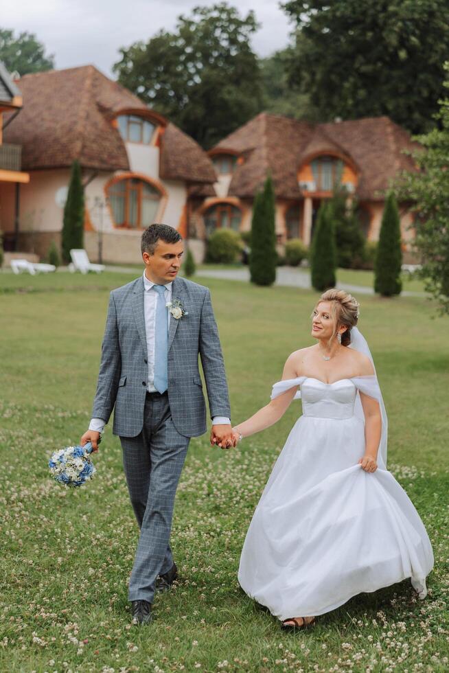 A handsome groom and an elegant bride in a lush white dress are walking in a summer park. Happy bride and groom getting ready for their best day. photo