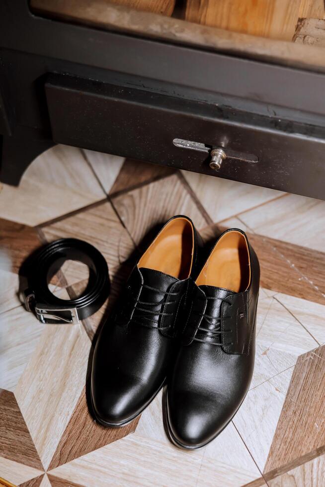 On the floor are men's dark leather shoes and a black belt, a man's suit on a mannequin, a wedding bouquet of flowers, wedding rings, men's perfume. Photo, top view. photo