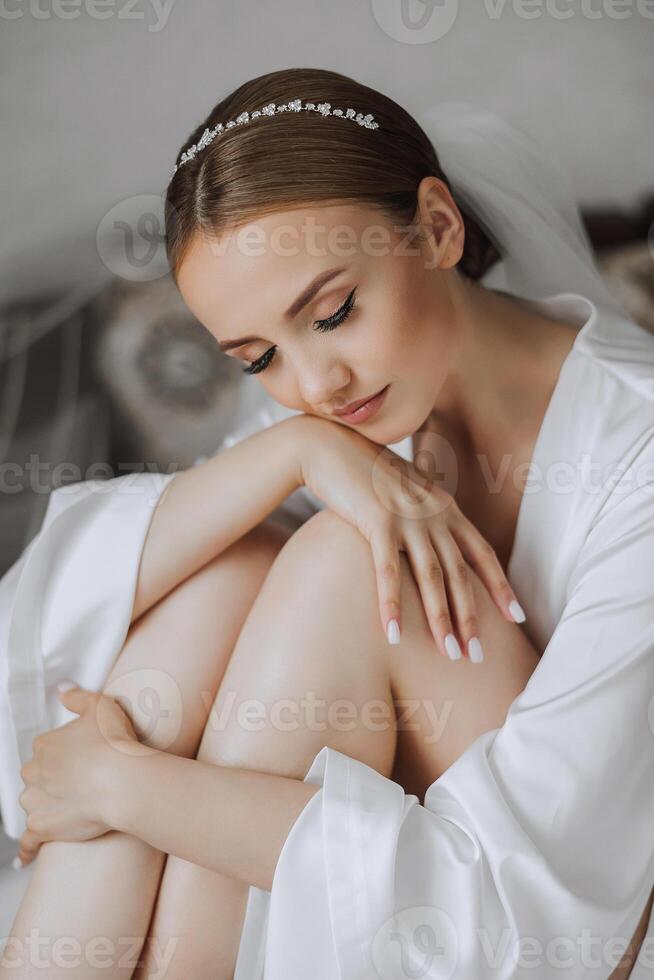 Beautiful bride in white wedding dress sitting on the bed in the morning. Fashion shot, beautiful woman in a dressing gown. Fashion, glamor concept photo