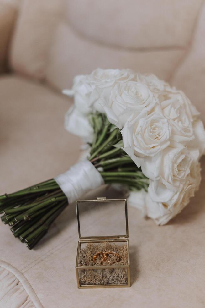 Wedding bouquet. White cut roses, green seed heads and leaves. Green stems and white ribbon and gold wedding rings. photo