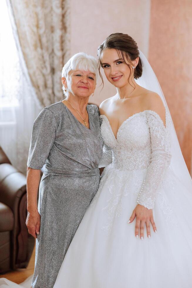 A beautiful and happy mother and her daughter, the bride, are standing next to each other. The best day for parents. Tender moments at the wedding. photo