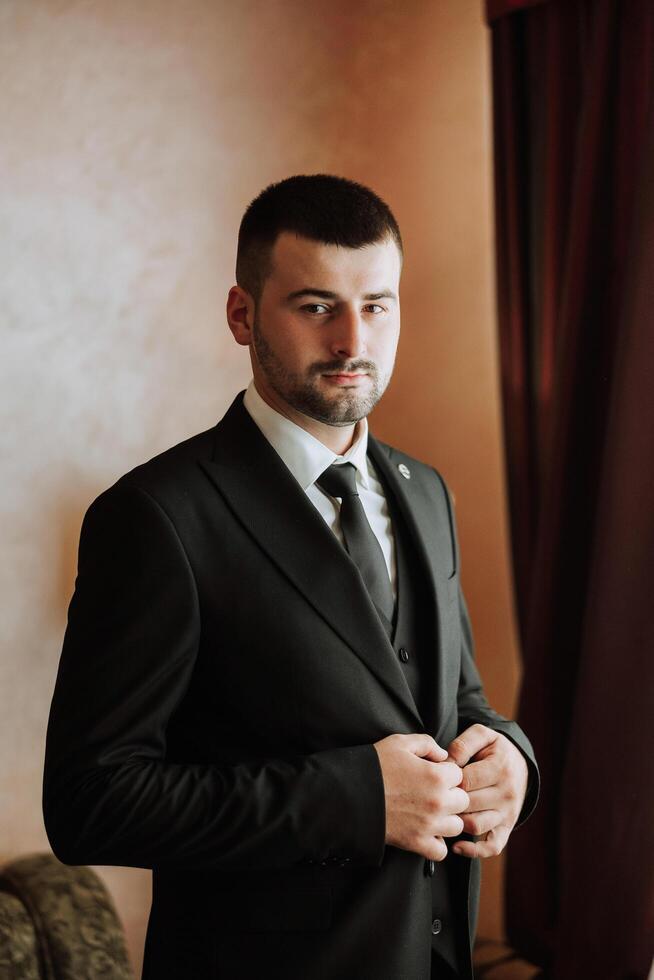 Portrait of a young groom at home before the wedding ceremony. A handsome man dressed in a classic suit. Male portrait. photo