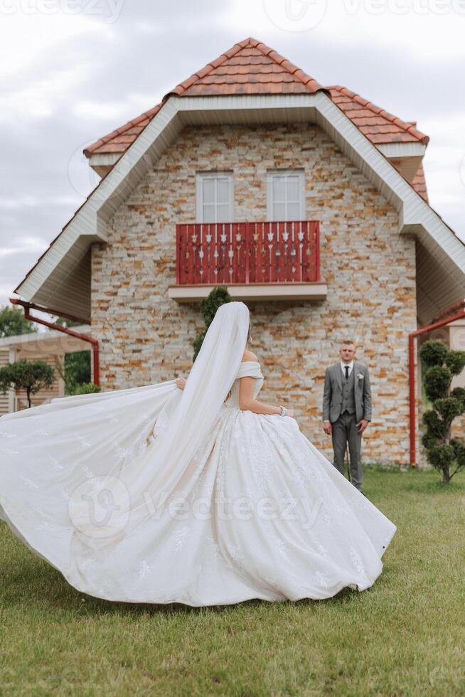 The bride is dressed in an elegant lush white wedding dress with a long veil and is ready for her groom. The first meeting of the bride and groom photo