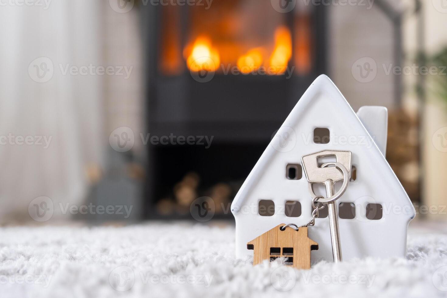 Key to house with keychain against background of fireplace stove with fire and firewood in Valentine decor, love home. Moving to new house, mortgage, rent and purchase real estate photo