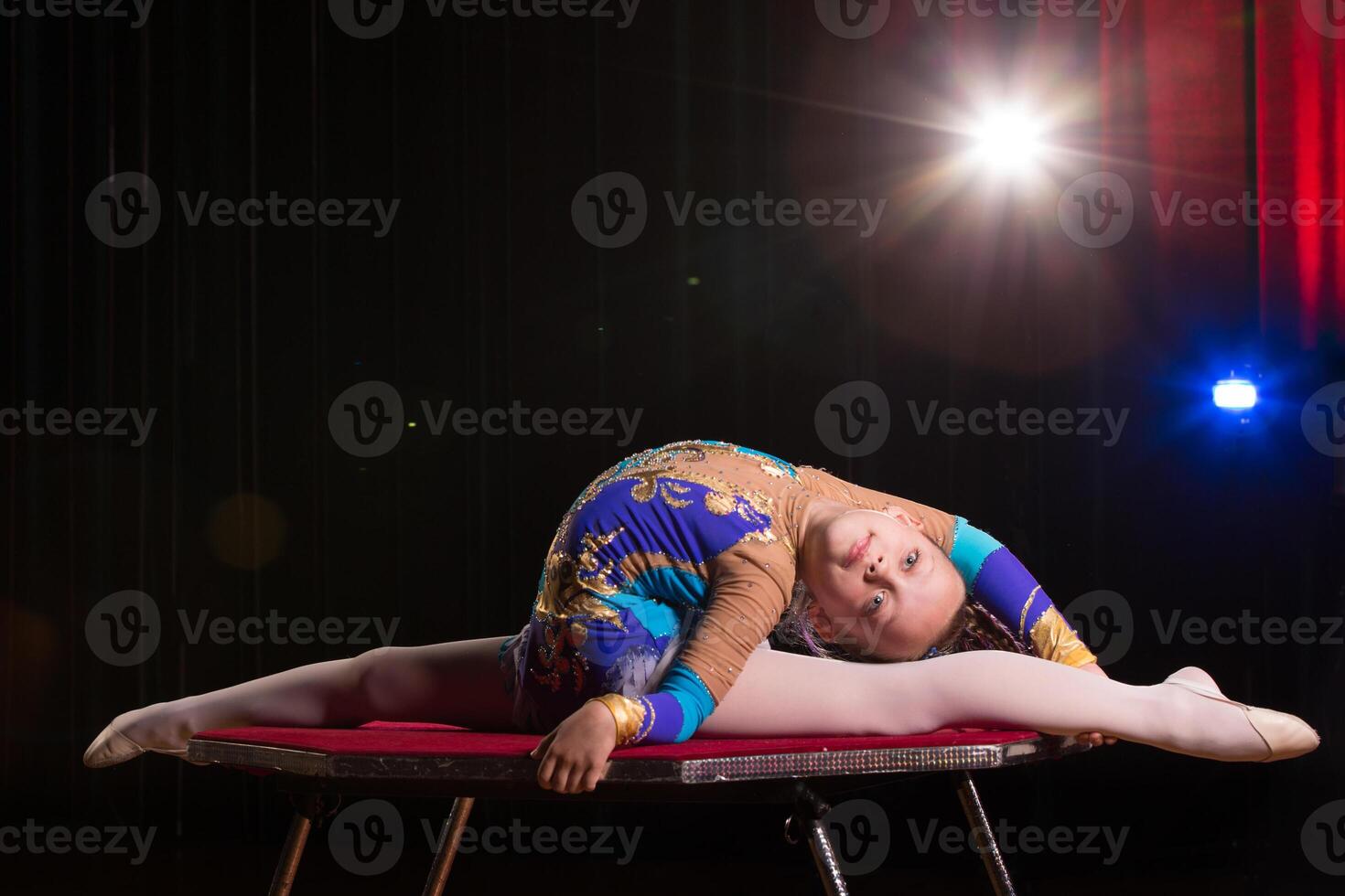 A girl with a flexible body. Performs a circus artist. Circus gymnast. Balancing act. The child performs an acrobatic trick photo