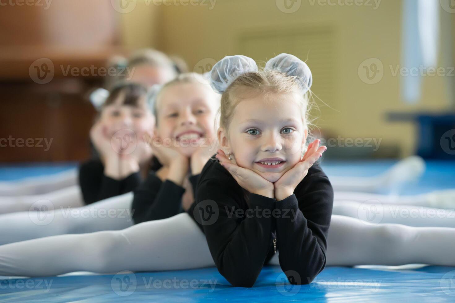 pequeño muchachas gimnastas sentar en el divisiones. niños hacer físico ejercicio. joven bailarinas.. formación de el inicial grupo en gimnasia.acrobacia lección foto